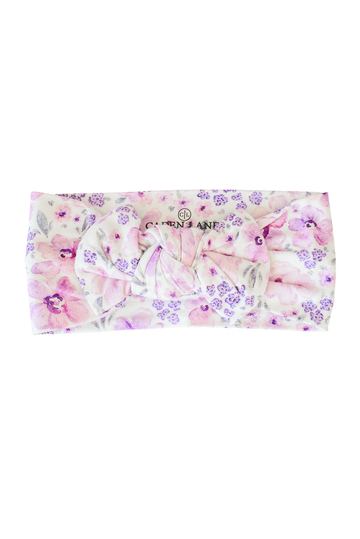 Flat lay of a Caden Lane white knit knotted bow headwrap in a Lilac Dreams print featuring pink watercolor blooms and tiny purple florals.