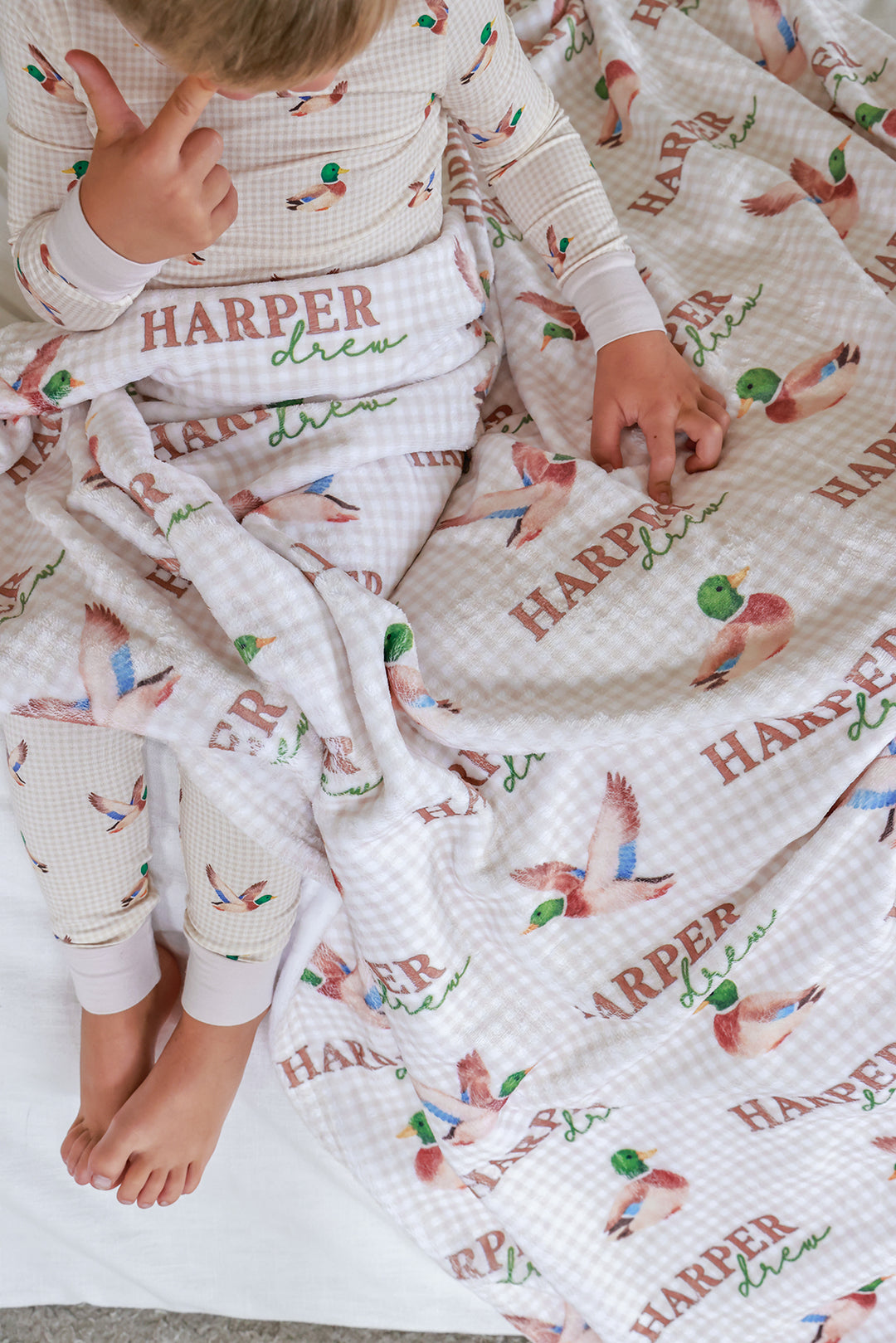 kid sitting on bed in little mallard pajamas with personalized blanket over lap 