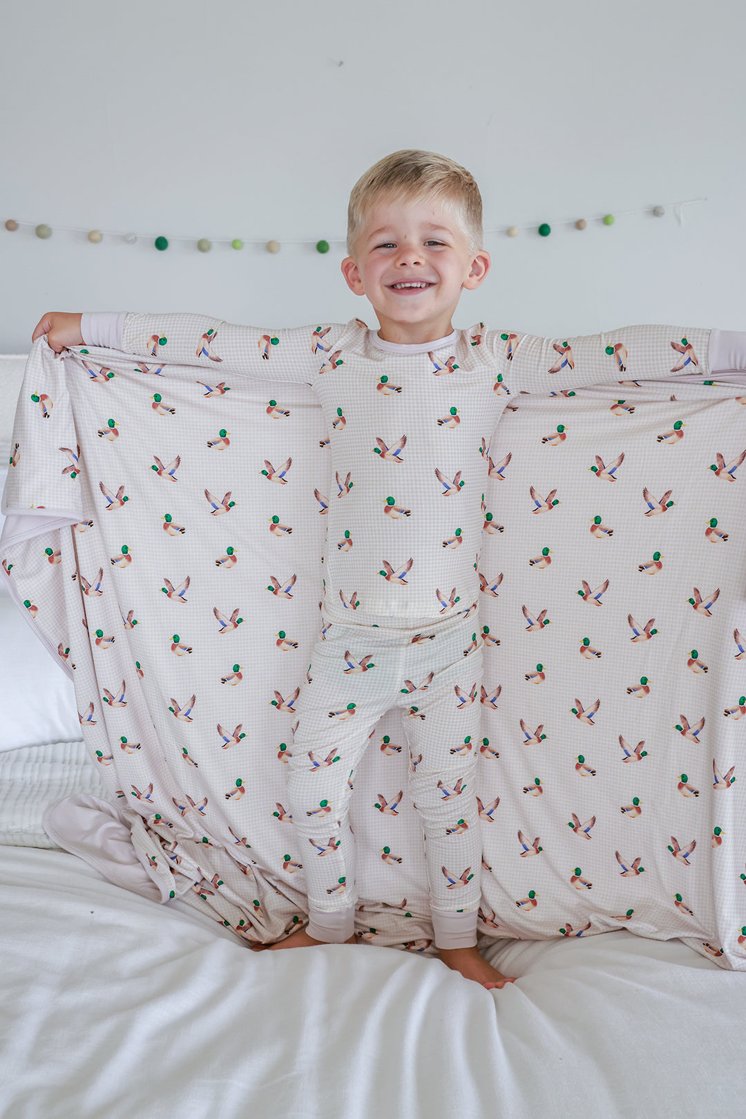 Toddler resting on bed with little mallard duck print double-sided bamboo blanket, showing mallard duck print pattern