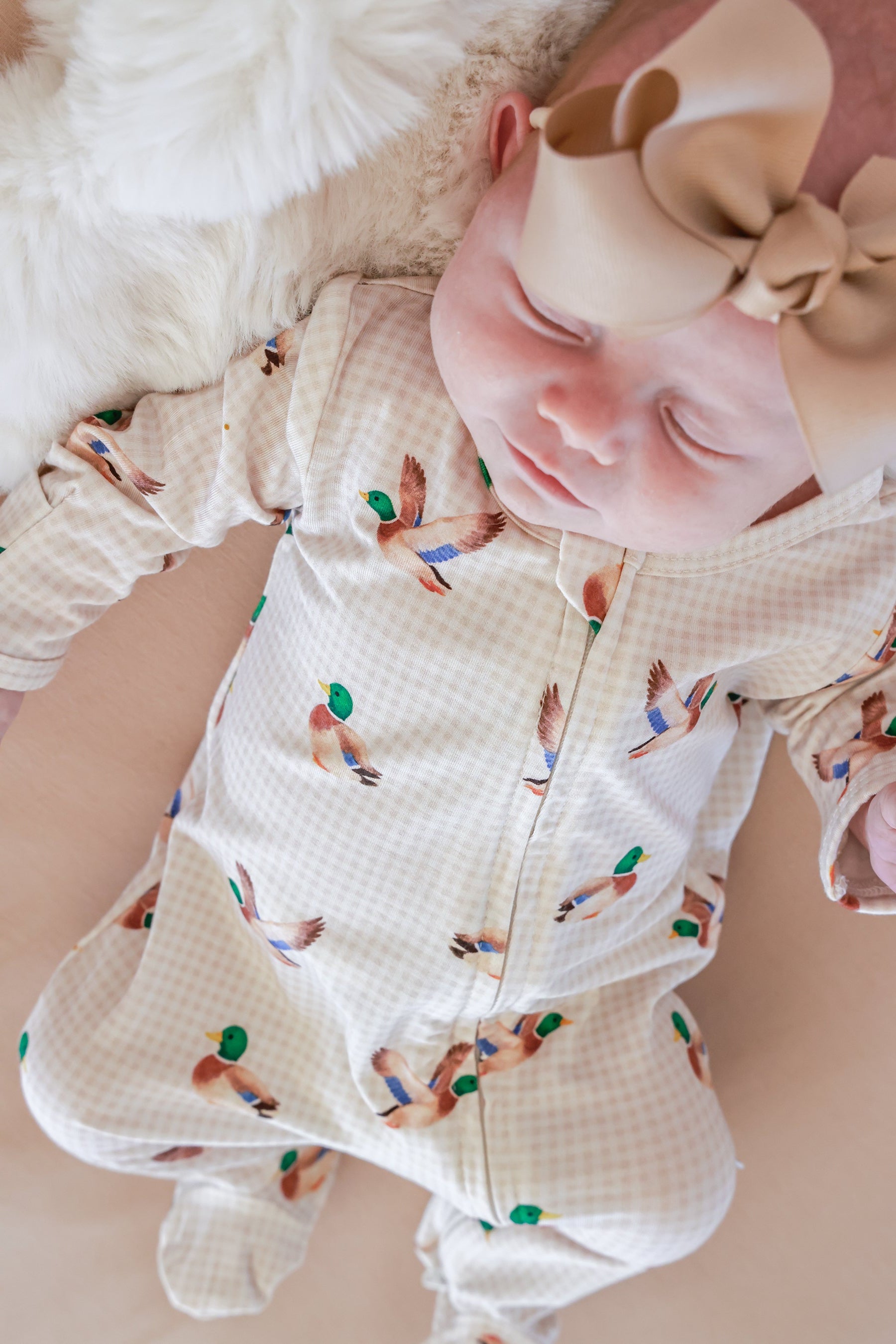 Sleeping newborn baby wearing little mallard duck print bamboo zipper footie, overhead view showing full garment
