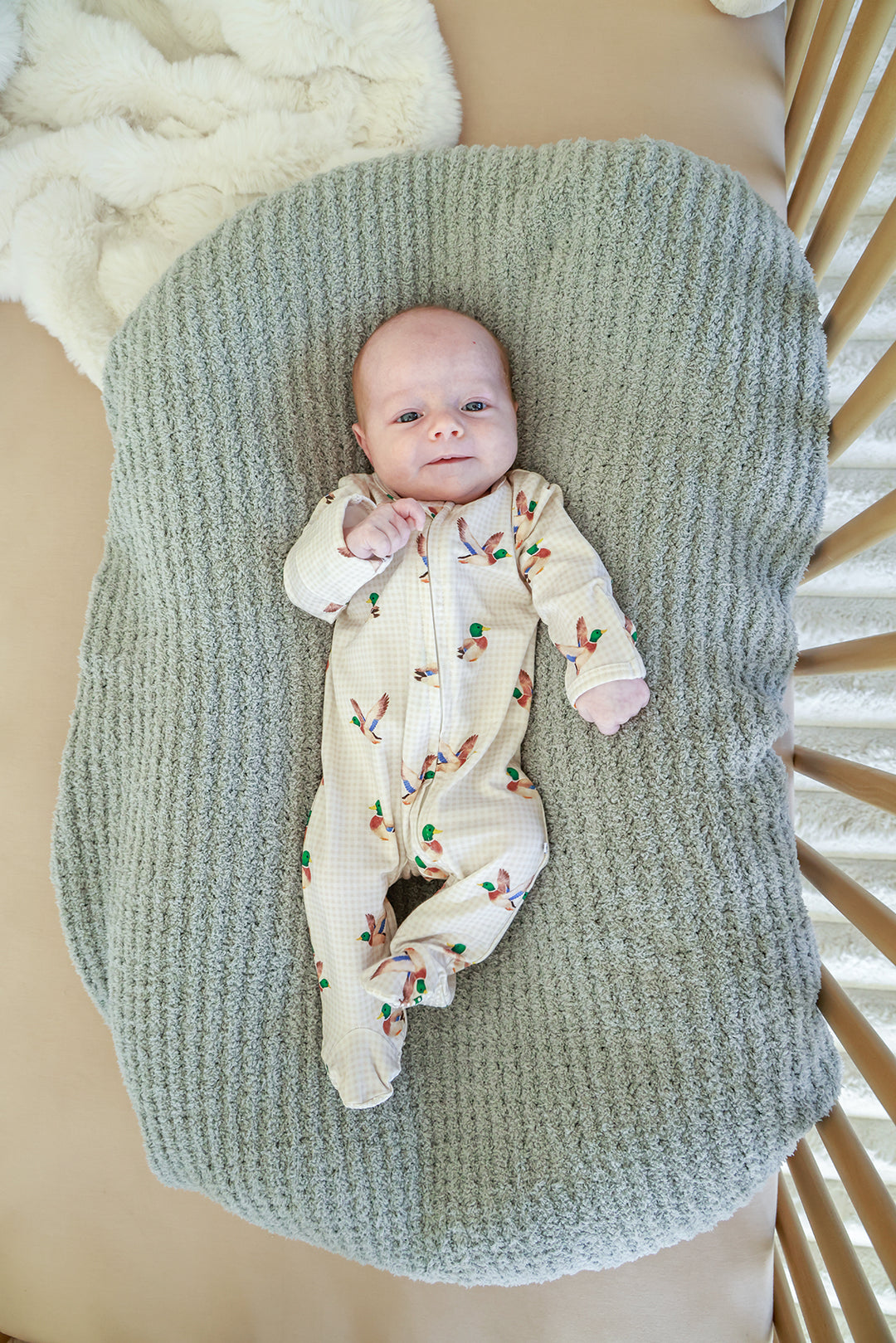 Newborn baby lying in crib wearing little mallard duck print bamboo zipper footie, overhead view from above
