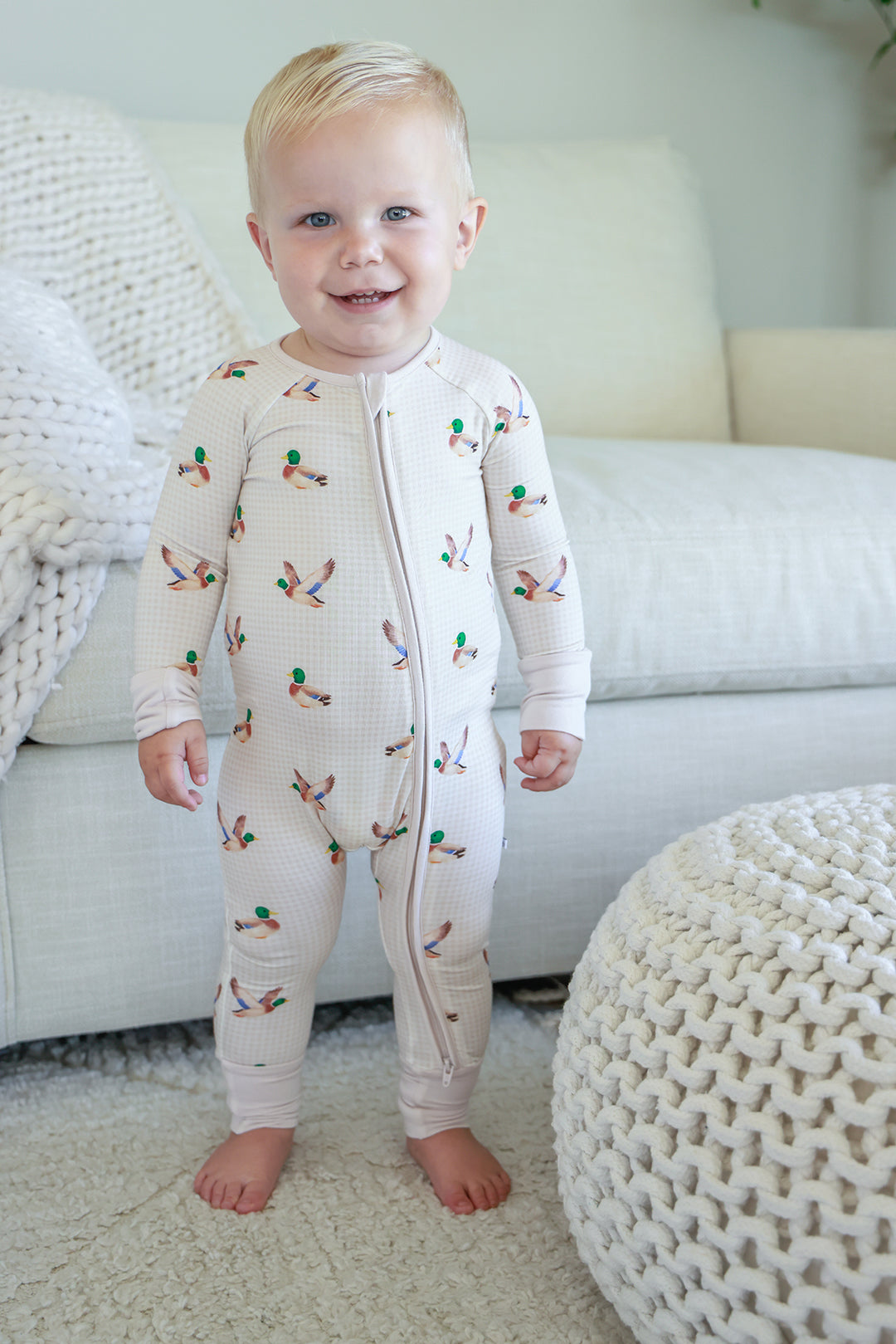 Toddler standing and smiling wearing little mallard duck print convertible zip romper, front view showing full-length zip and duck print