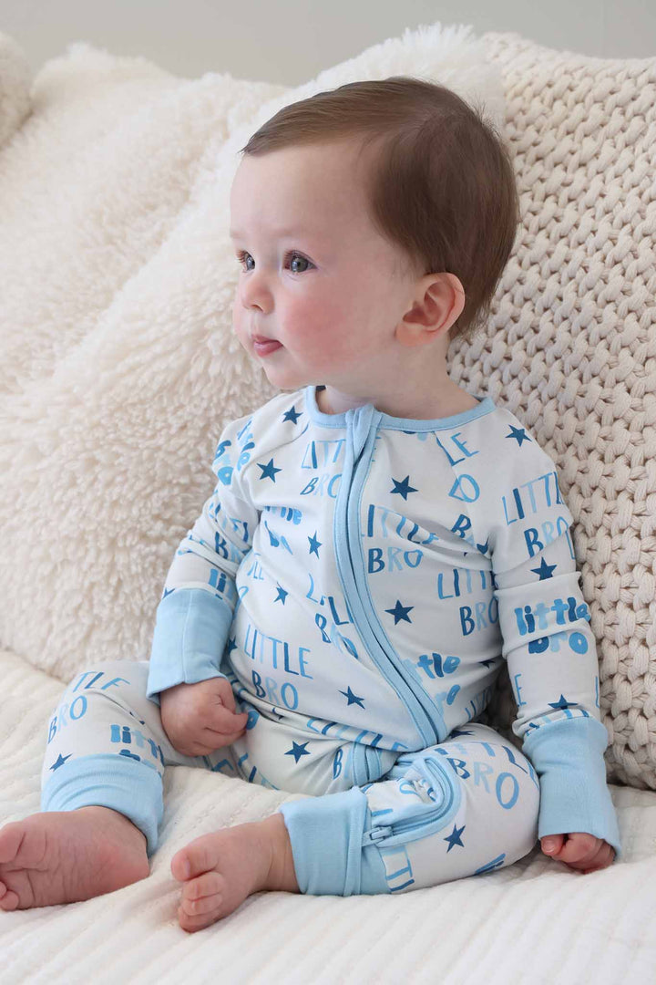 boy sitting on bed looking to the side wearing the blue little bro convertible zip romper pajama 