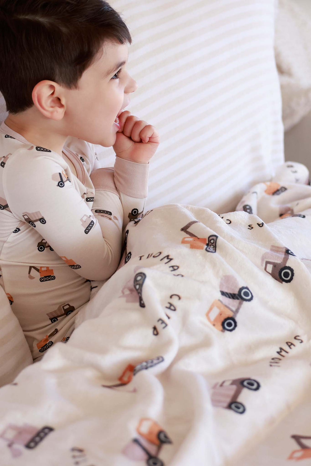 side view of boy wearing long sleeve little builder pajama set with matching personalized blanket on his lap