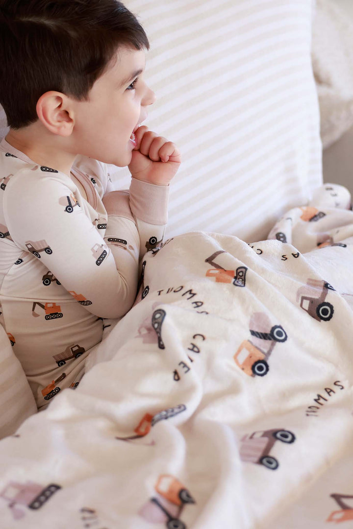 side view of boy wearing long sleeve little builder pajama set with matching personalized blanket on his lap