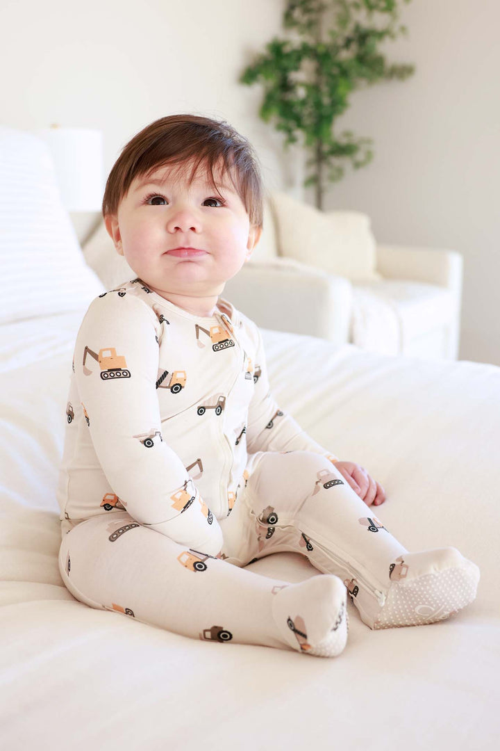 sitting baby boy wearing neutral construction bamboo zipper footie