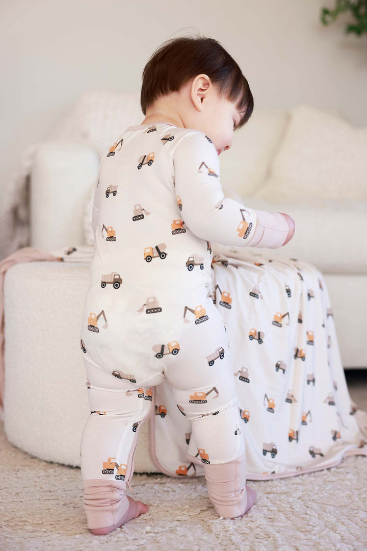 baby boy leaning on ottoman wearing little builder convertible zip romper