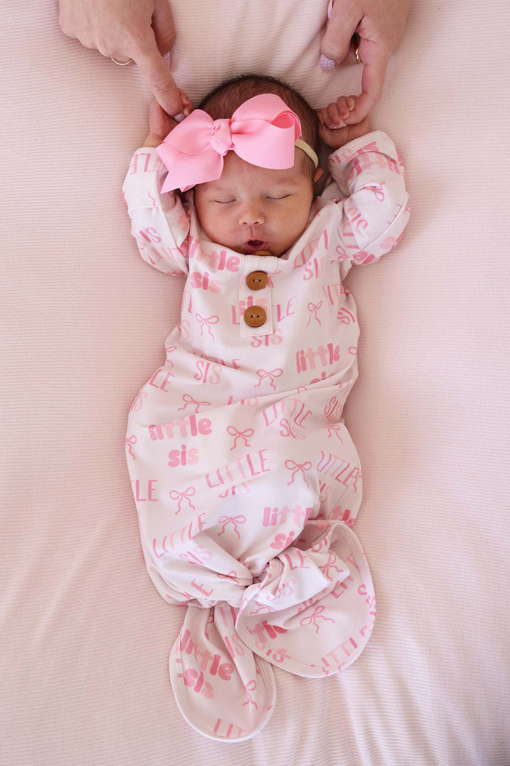baby girl wearing little sis bow newborn knot gown and hat set wearing a matching pink ribbon bow headband 