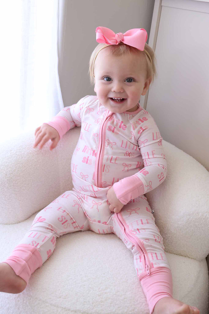 happy baby girl sitting on chair in little sis convertible zip romper with matching bright pink ribbon bow headband 