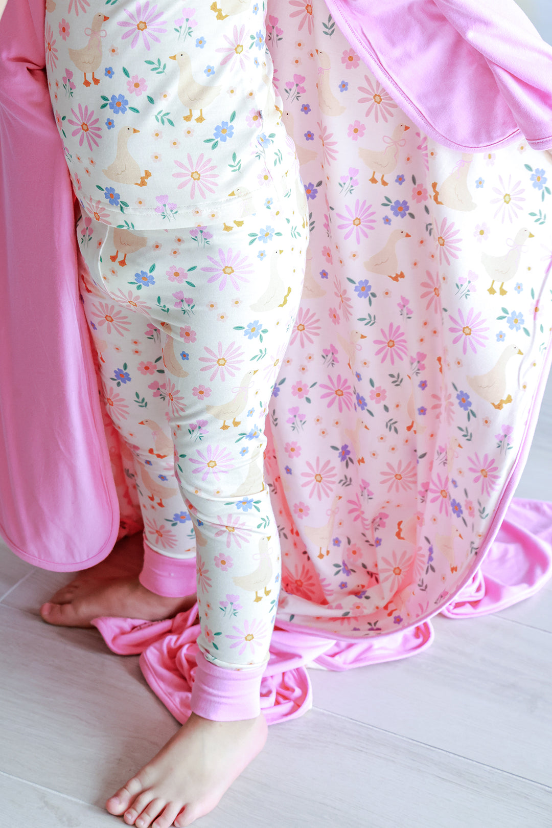 Lifestyle detail photo showing the Double Sided Bamboo Blanket in the Lucy Goosy floral print with the pink solid reverse side, styled with matching Lucy Goosy print pajamas