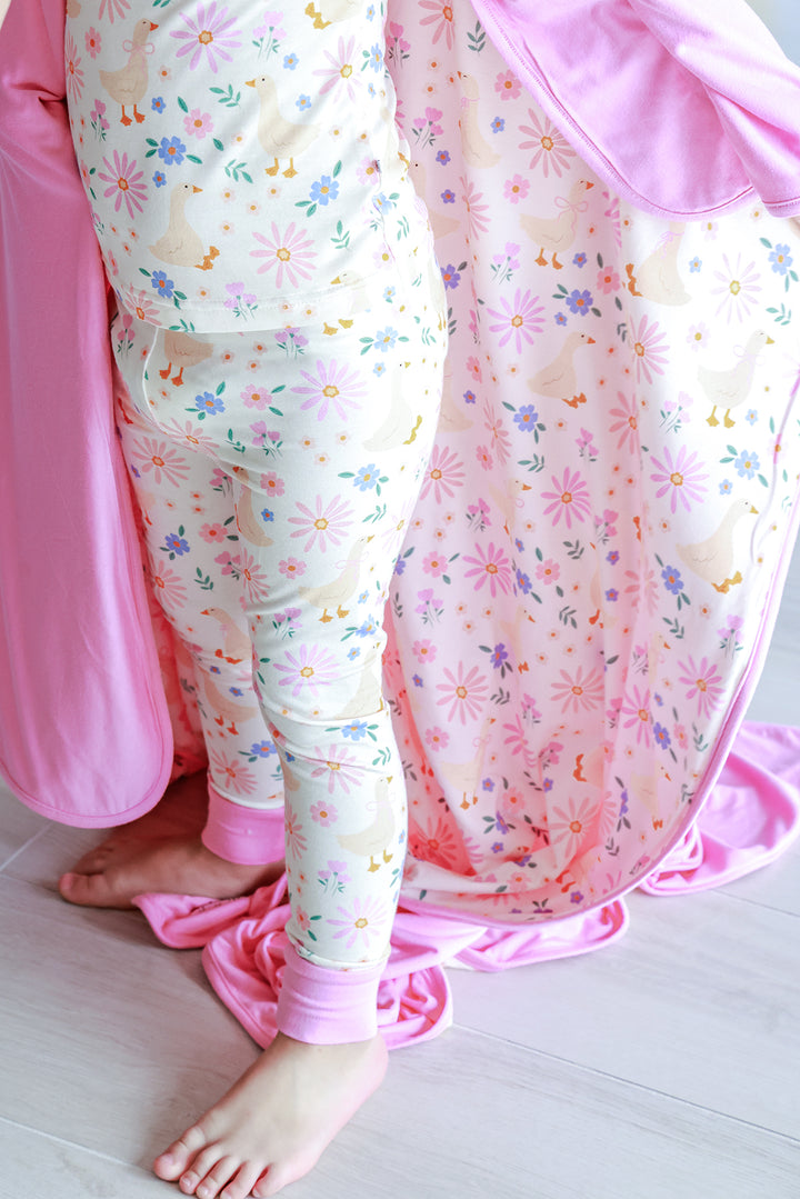 Lifestyle detail photo showing the Double Sided Bamboo Blanket in the Lucy Goosy floral print with the pink solid reverse side, styled with matching Lucy Goosy print pajamas