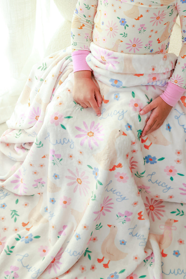 Lifestyle photo of child with the Personalized Kids Blanket in the Lucy Goosy floral print draped over them, showing name Lucy printed throughout the design