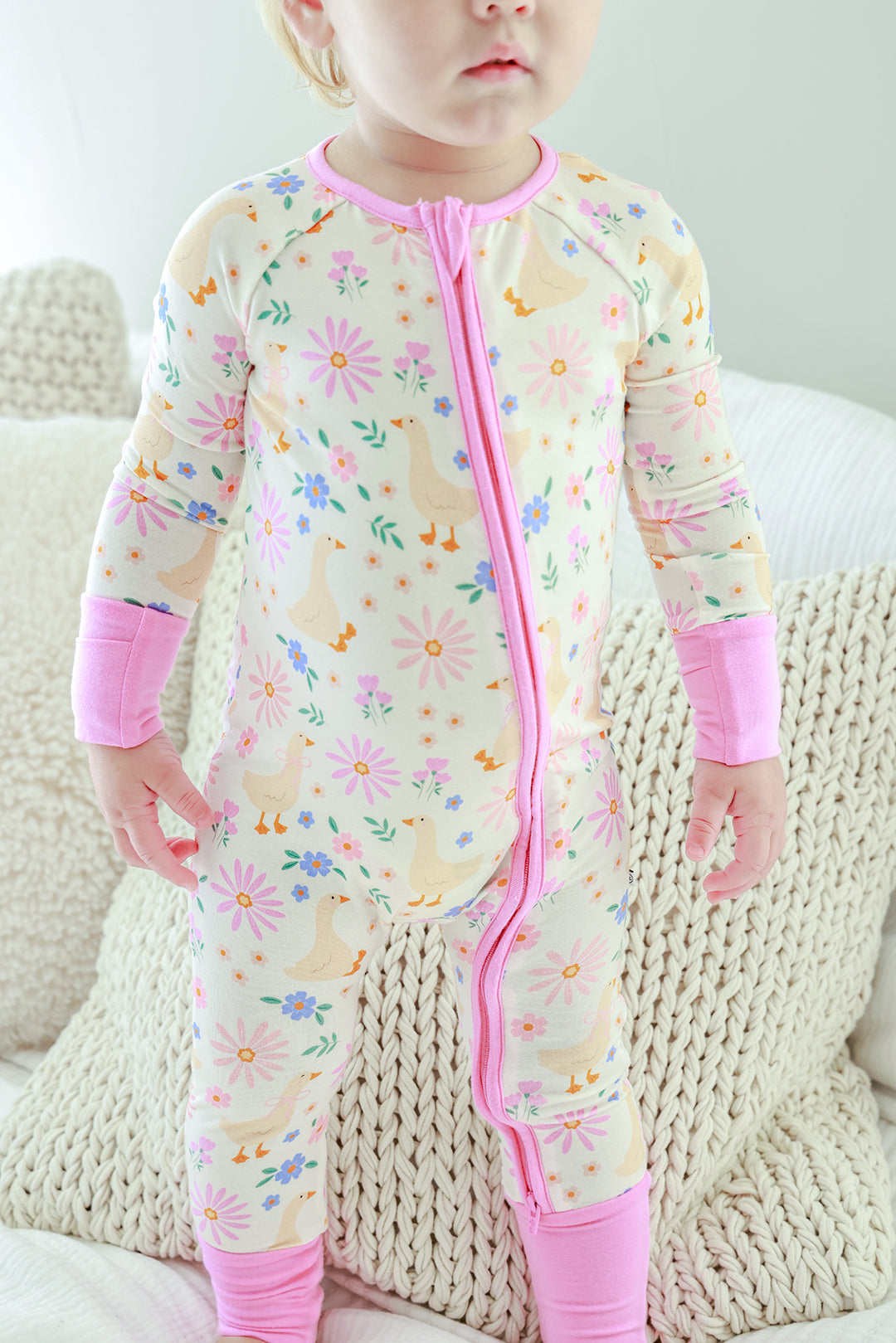 Toddler wearing the Lucy Goosy Convertible Zip Romper in the floral print with pink zipper and trim, standing on a knit textured surface, lifestyle photo