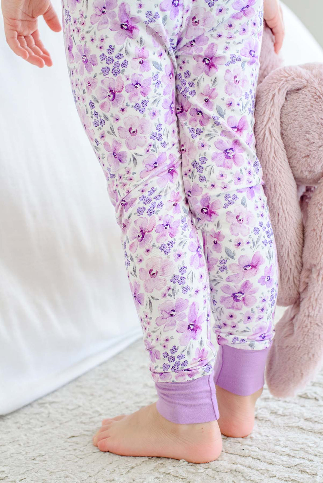 Back view of a girl's legs in Caden Lane cream knit pajama pants in a Lilac Dreams print featuring watercolor flowers, with lilac ankle cuffs.