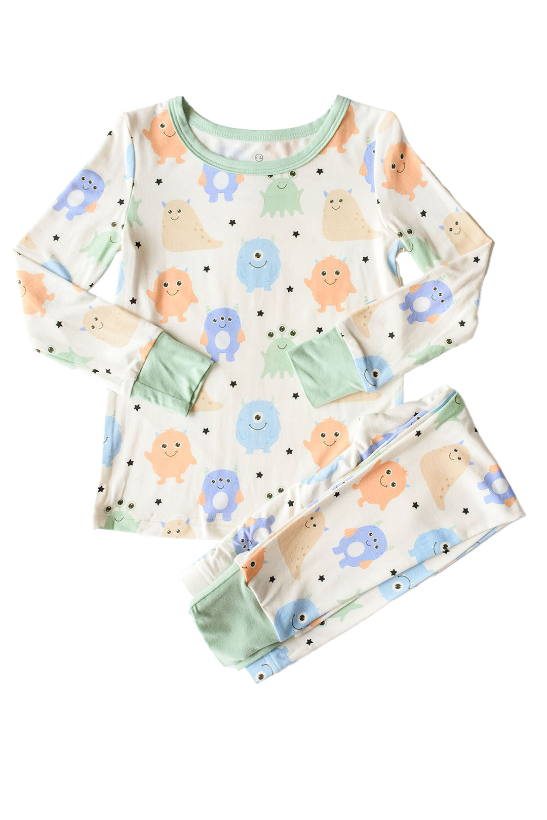 Flat lay of a Caden Lane Little Monsters two-piece pajama set with sage green trim, showing blue, green, and orange cartoon monsters on cream fabric
