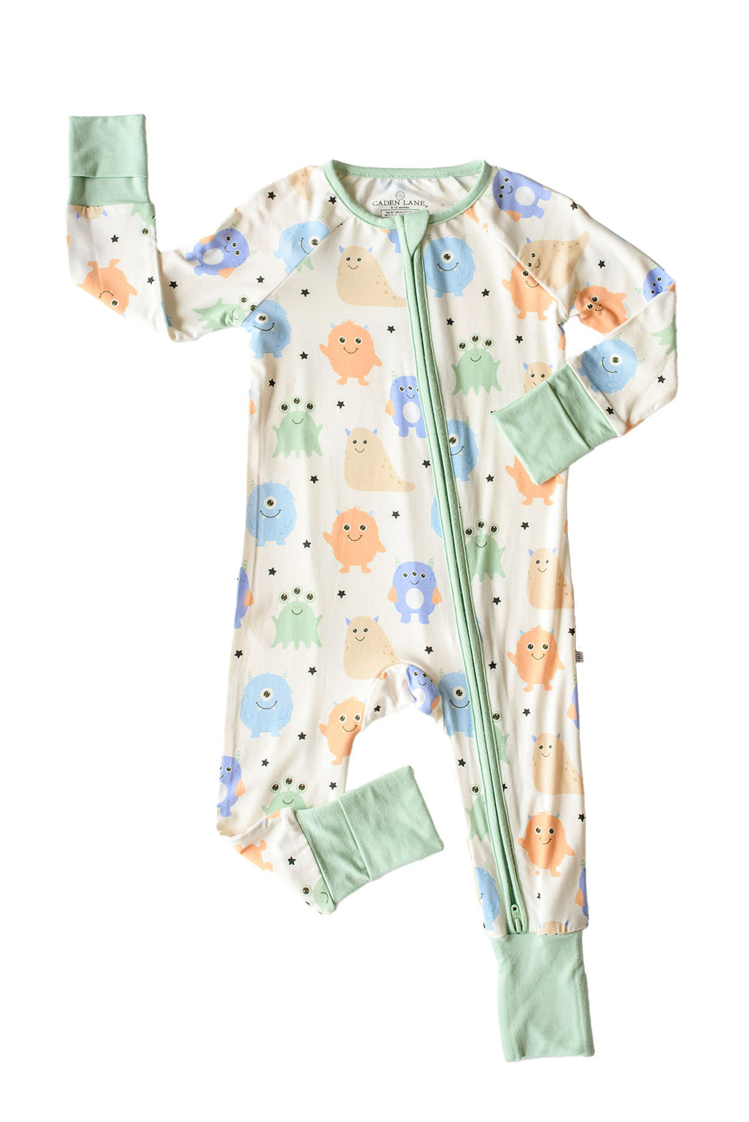 Flat lay of a Caden Lane Little Monsters zipper footie with sage green trim, showing blue, green, and orange cartoon monsters on cream fabric