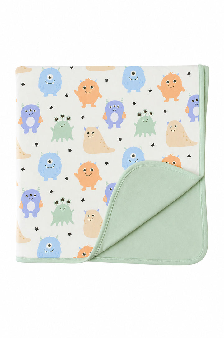 Flat lay of a Caden Lane Little Monsters bamboo blanket, folded to show cream monster print front and sage green reverse side