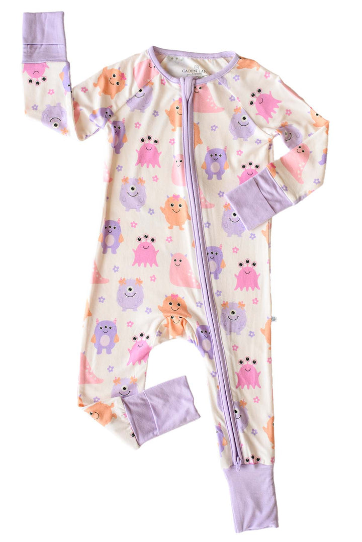 Flat lay of a Caden Lane Little Monsters zipper footie with lavender trim, showing pink, purple, and orange cartoon monsters and floral accents