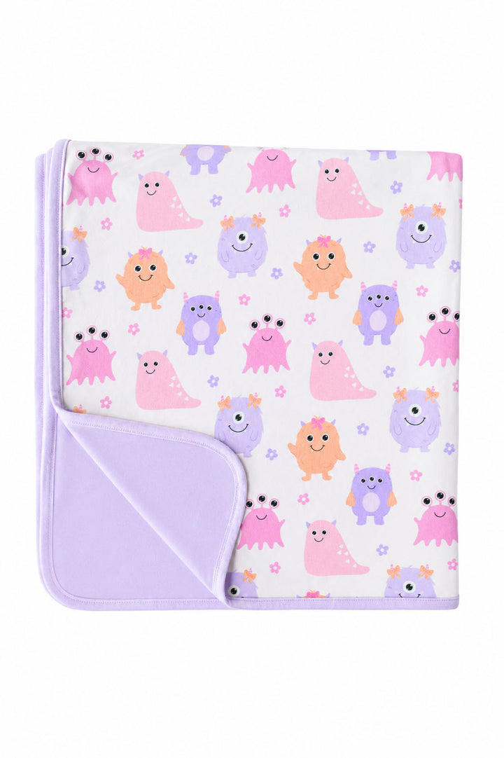 Flat lay of a Caden Lane Little Monsters bamboo blanket, folded to show cream monster print front and lavender reverse side