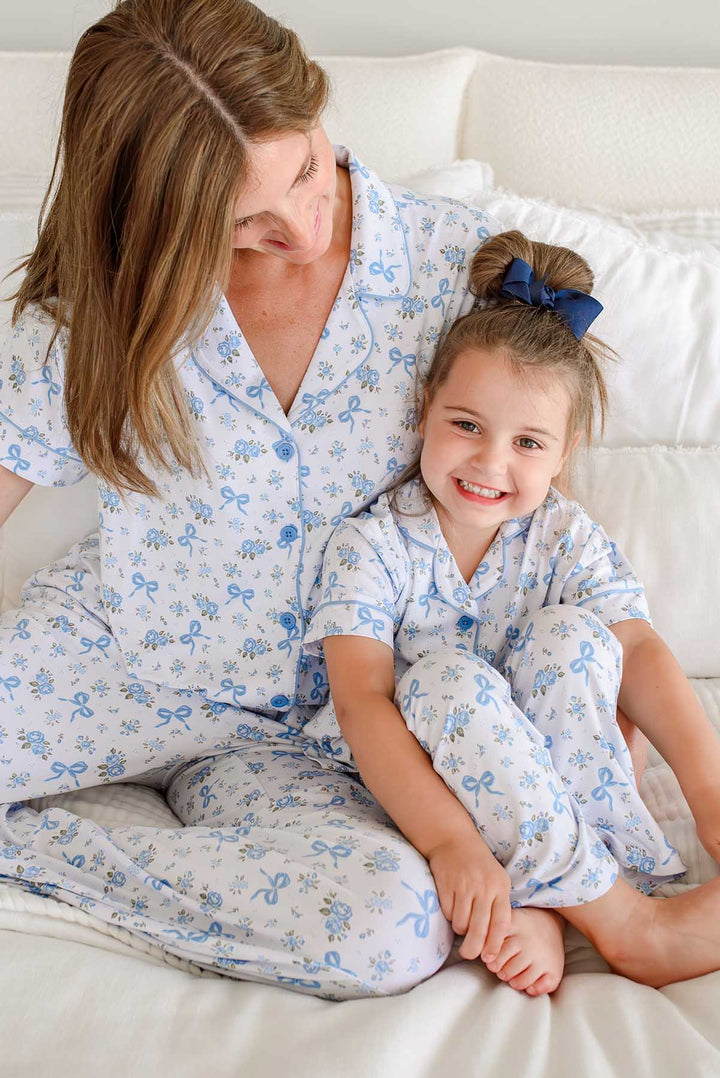 Mother and daughter sitting on a bed smiling, both wearing matching Tied In Blooms bamboo lounge sets in blue floral and bow print
