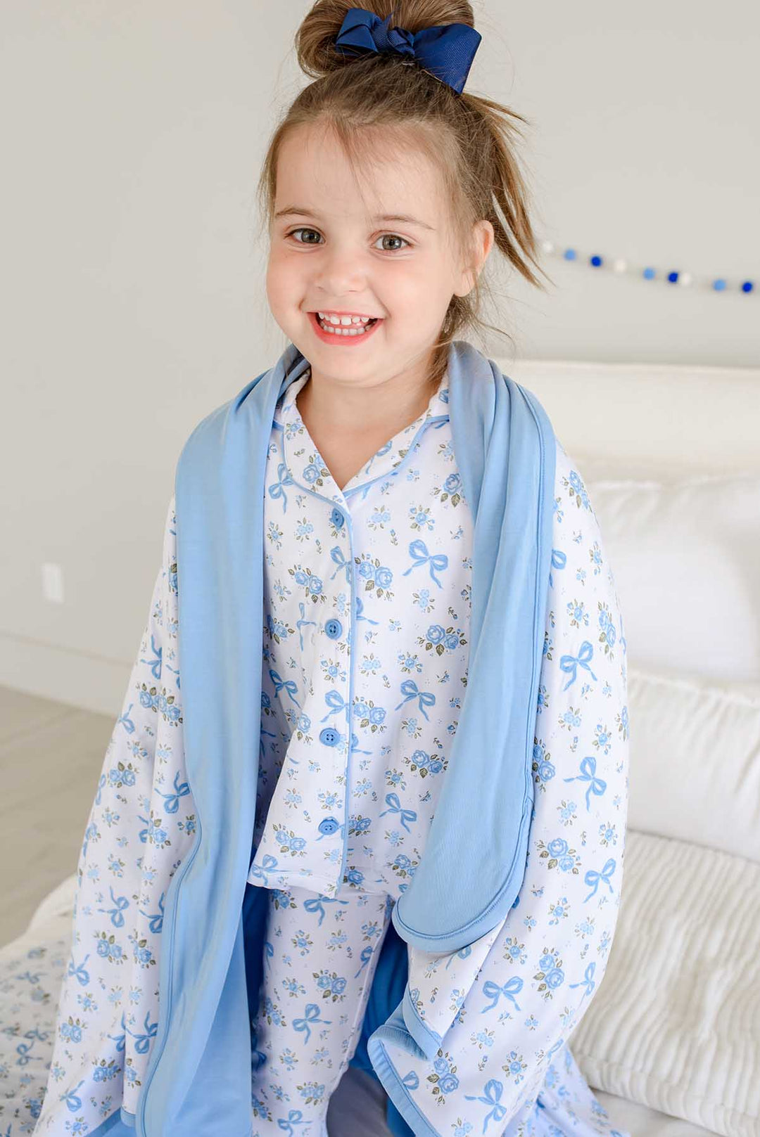 Laughing girl with a bow in her hair, draped with a Tied In Blooms double sided bamboo blanket in blue floral and bow print