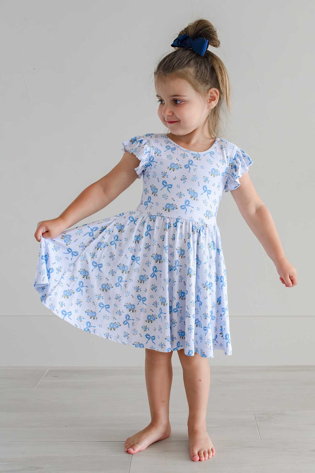 Joyful girl swaying in a Tied In Blooms ruffle twirl dress with blue floral and bow print