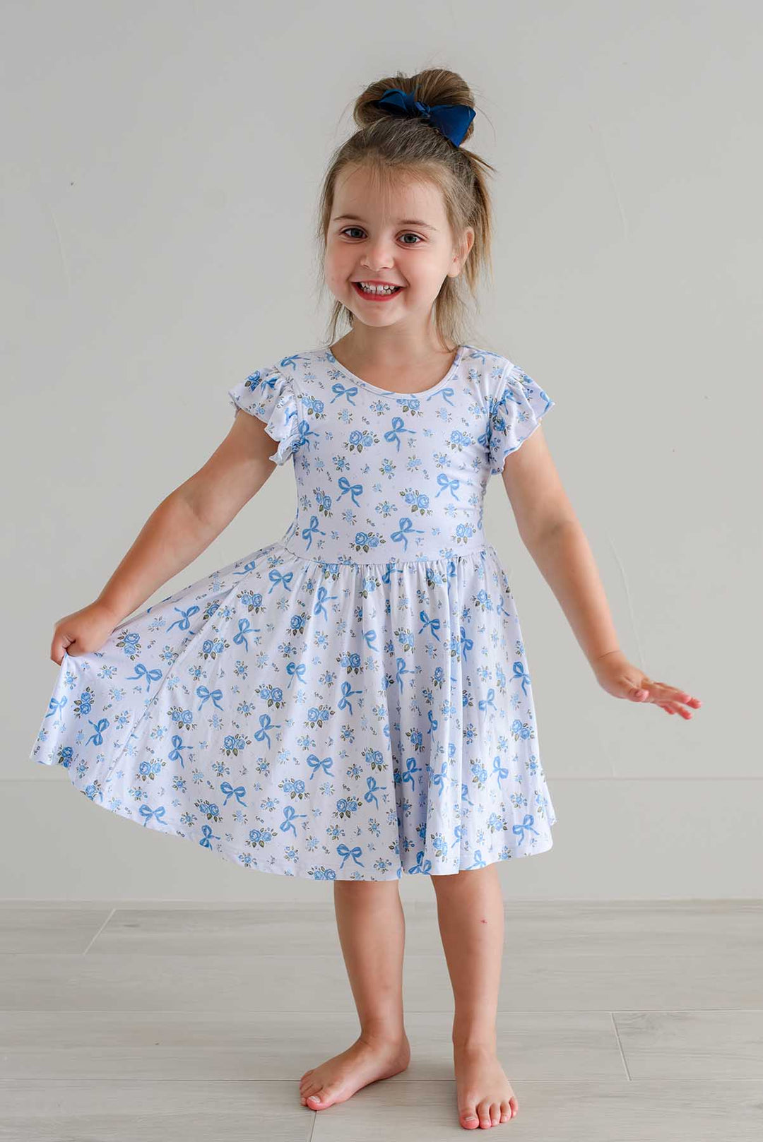 Smiling girl twirling in a Tied In Blooms ruffle twirl dress with blue floral and bow print