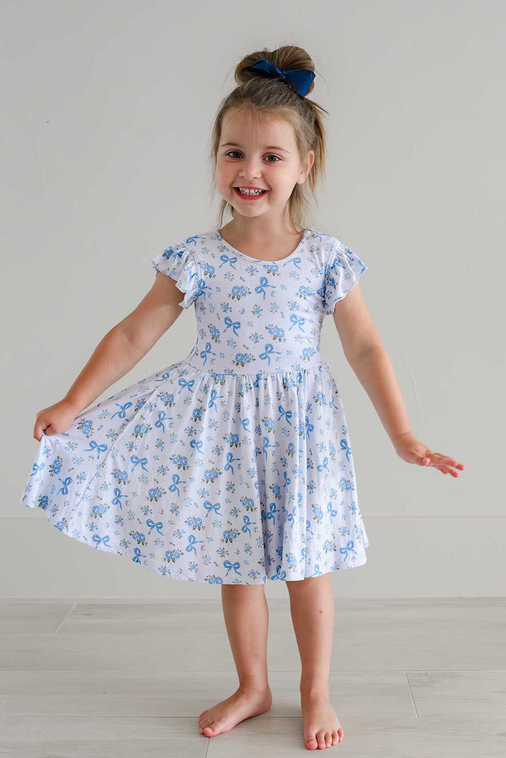 Smiling girl twirling in a Tied In Blooms ruffle twirl dress with blue floral and bow print