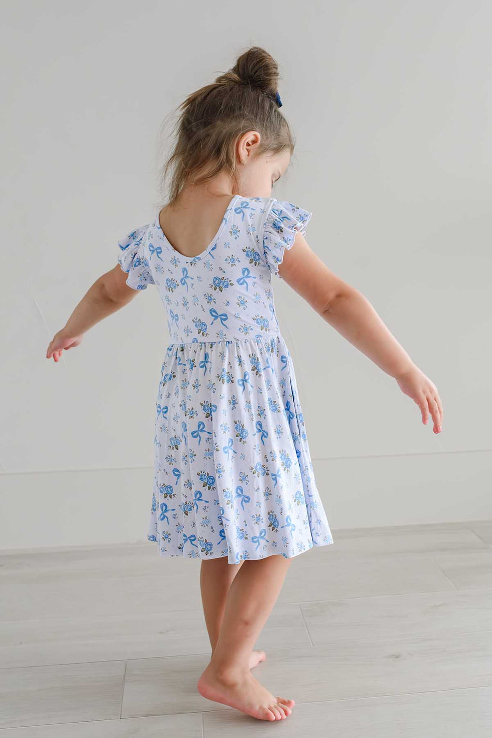 Girl swishing the skirt of a Tied In Blooms ruffle twirl dress with blue floral and bow print