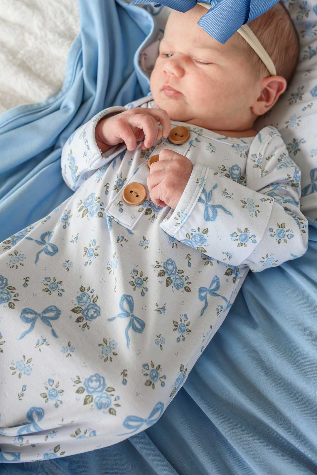 Sleeping baby with a blue bow headband wearing a Tied In Blooms knot gown in blue floral and bow print