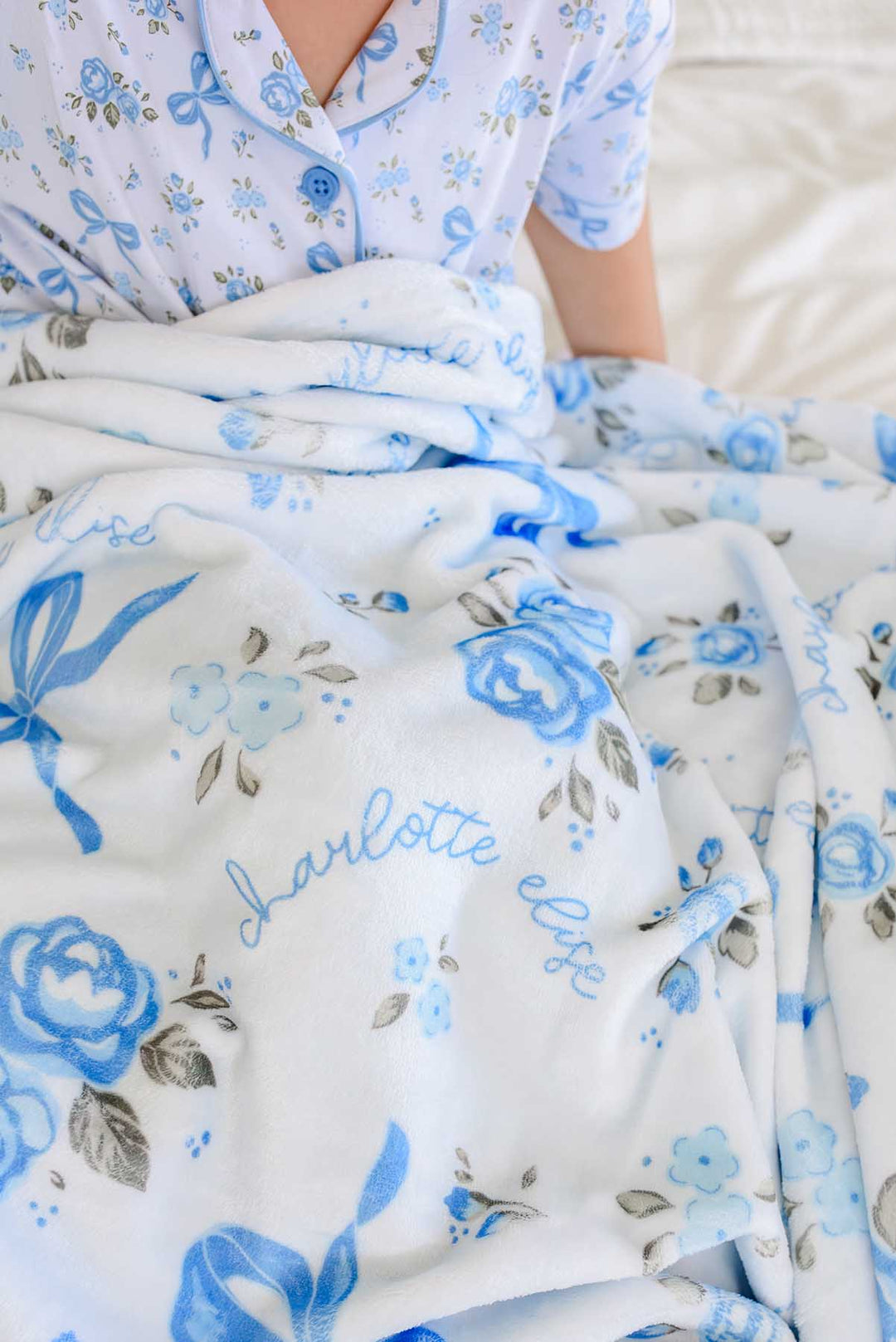 Close-up of a Tied In Blooms personalized blanket in blue floral and bow print, showing the name Charlotte Elise in cursive script