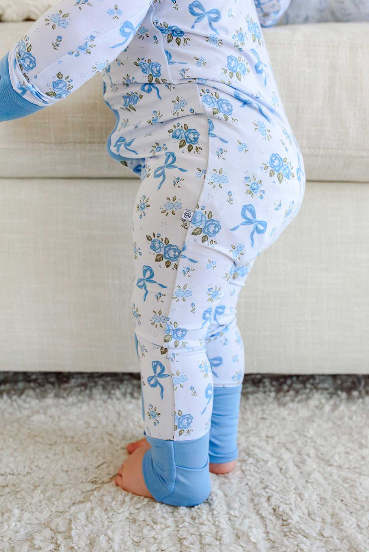 Close-up back view of a baby wearing a Tied In Blooms convertible bamboo zip romper in blue floral and bow print with solid blue footie cuffs