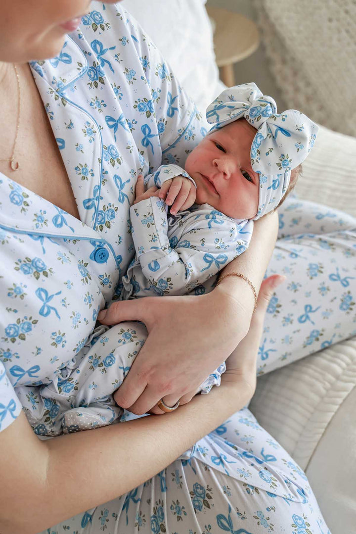 Mother cradling her baby, both dressed in matching Tied In Blooms attire in blue floral and bow print with a bow headwrap
