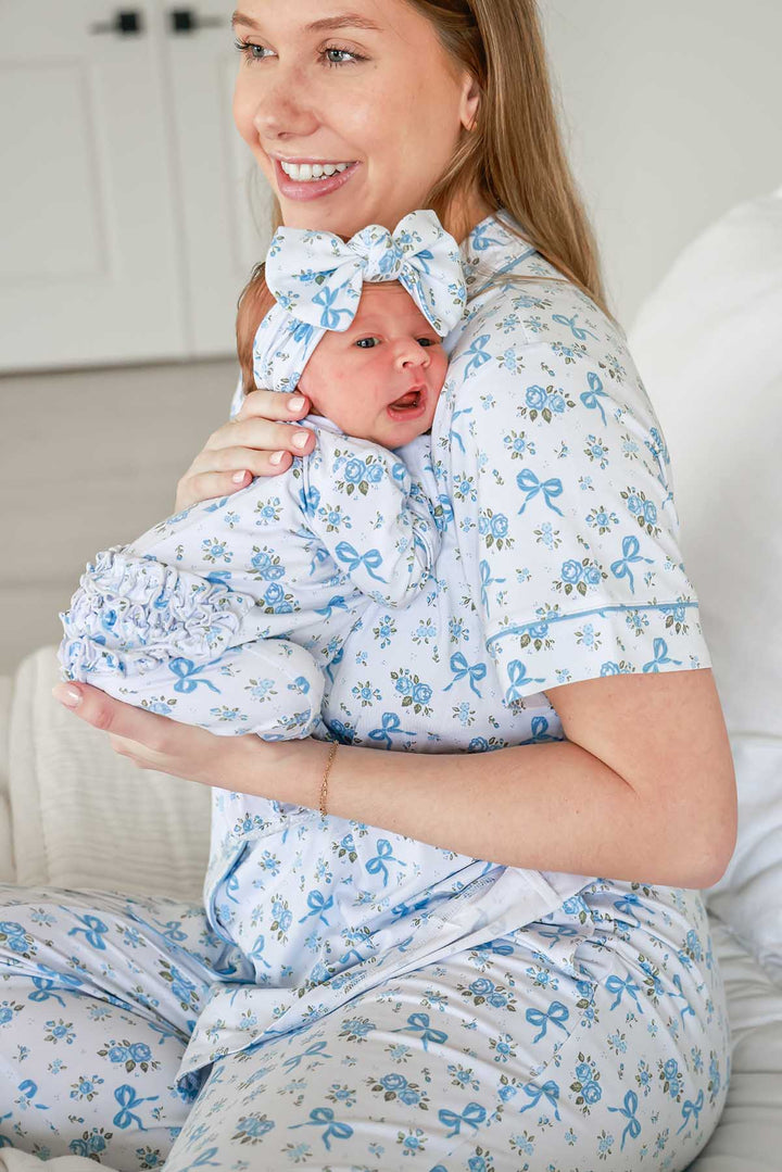 Mother holding her baby, both wearing matching Tied In Blooms pajamas in blue floral and bow print with a bow headwrap