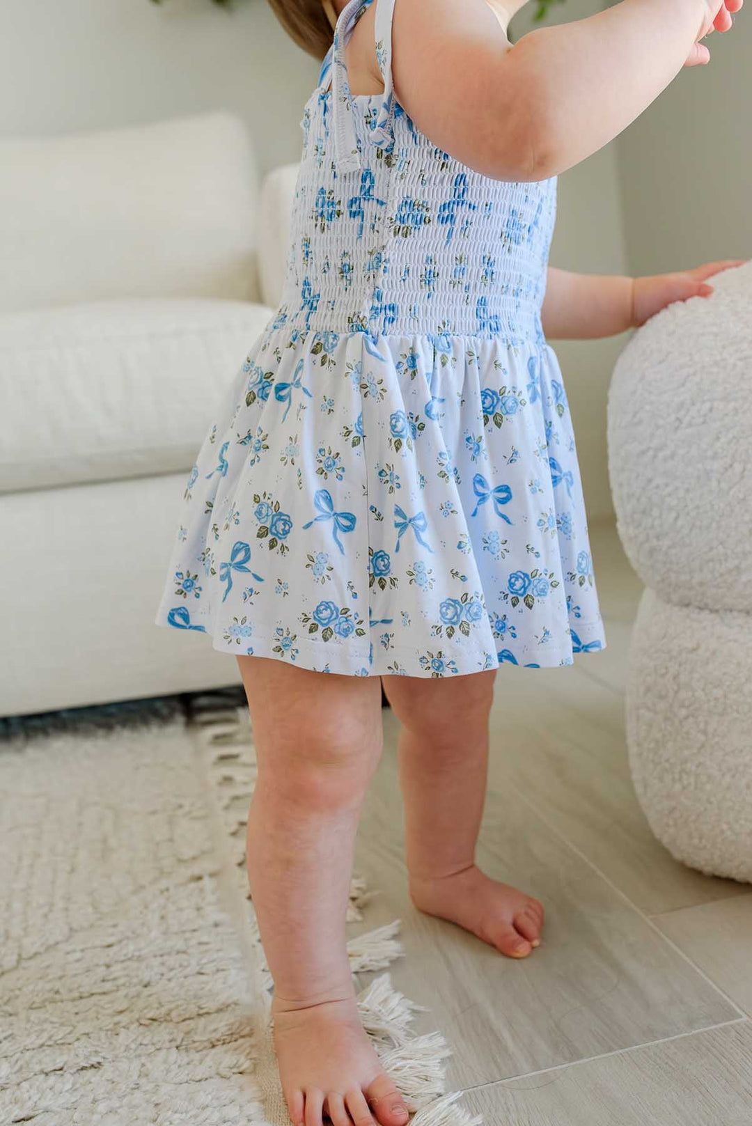 Toddler standing showing the twirl skirt of a Tied In Blooms smocked bodysuit in blue floral and bow print