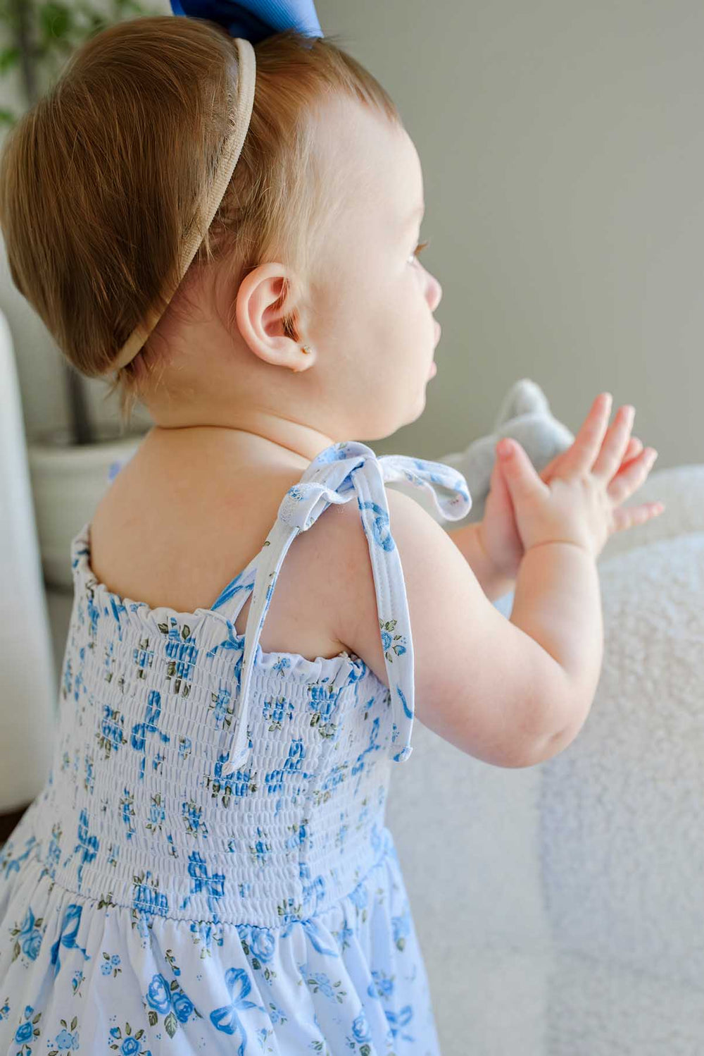 Close-up of a toddler's shoulder wearing a Tied In Blooms smocked twirl bodysuit in blue floral and bow print, showing the tie strap