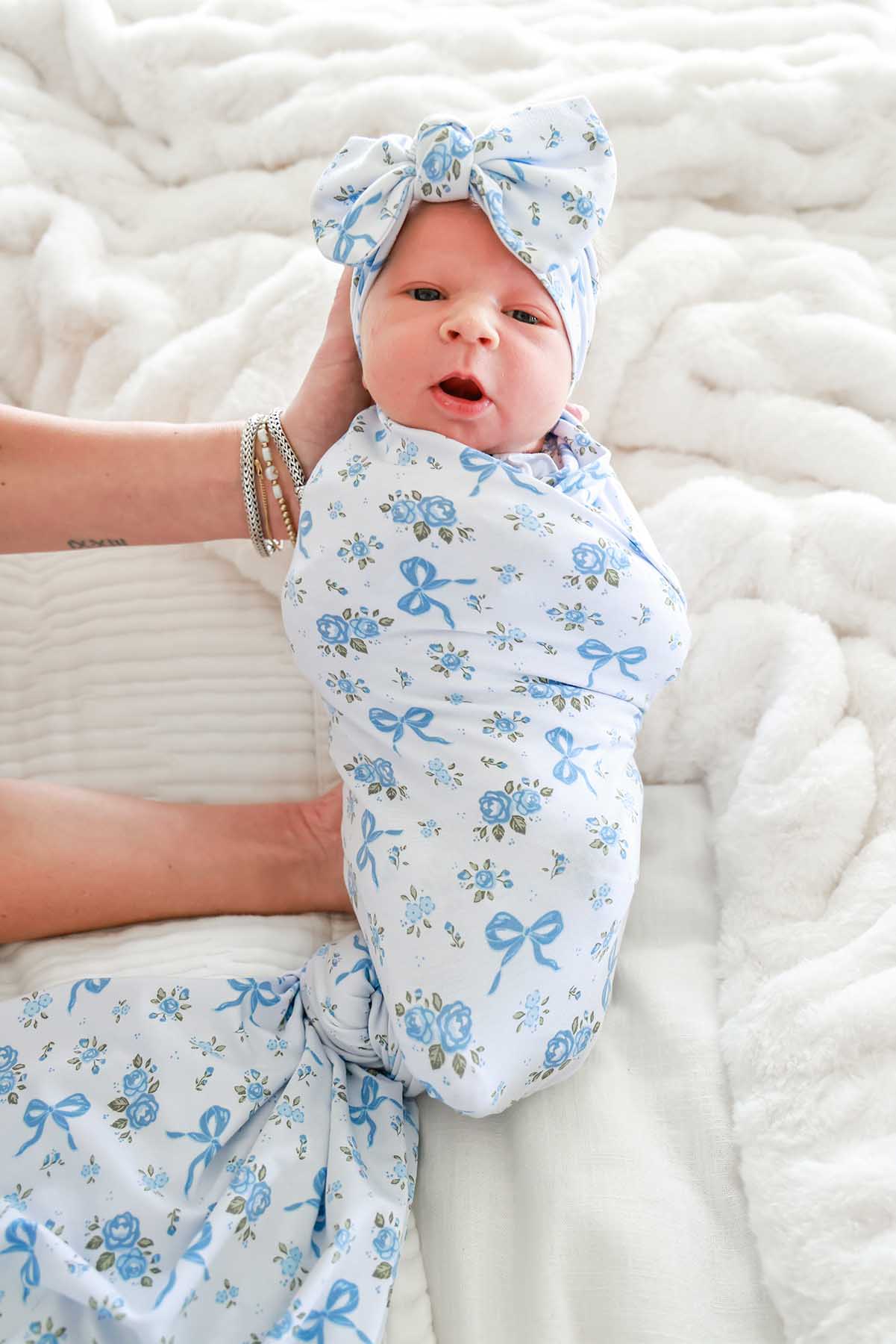 Newborn baby wearing a Tied In Blooms bow headwrap, swaddled in matching blue floral and bow print fabric