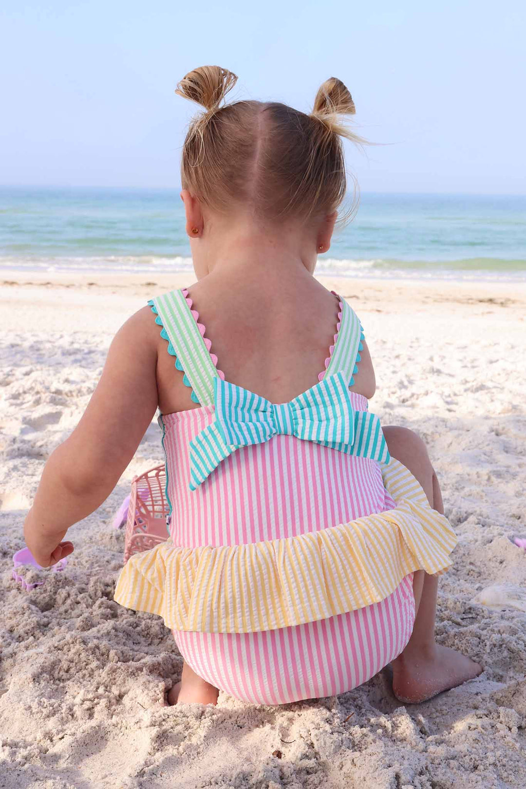 girl playing in the sand in color block seersucker one piece swimsuit with bow on back 