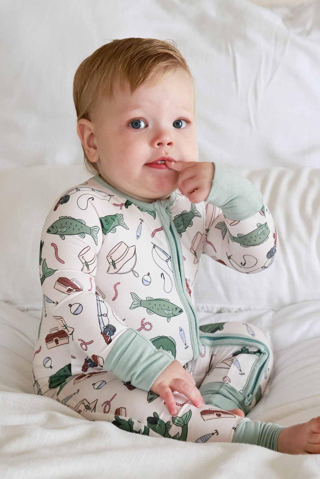 Baby sitting on bed wearing the Off The Hook convertible zip romper with fishing themed print close-up view
