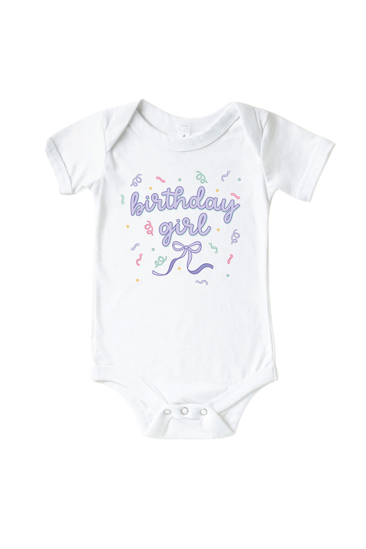 Caden Lane Birthday Bash white baby bodysuit with "birthday girl" in purple script, a bow, and confetti accents.