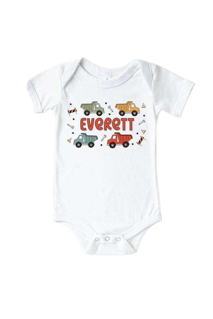 Flat lay of a Caden Lane white short-sleeve bodysuit in a Busy Builder print featuring sage, mustard, blue, and red dump trucks, reading "Everett" in red letters.