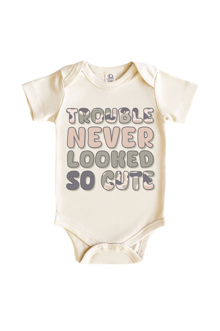 Natural cream baby onesie bodysuit with "Trouble Never Looked So Cute" slogan in pink and gray camo-style lettering