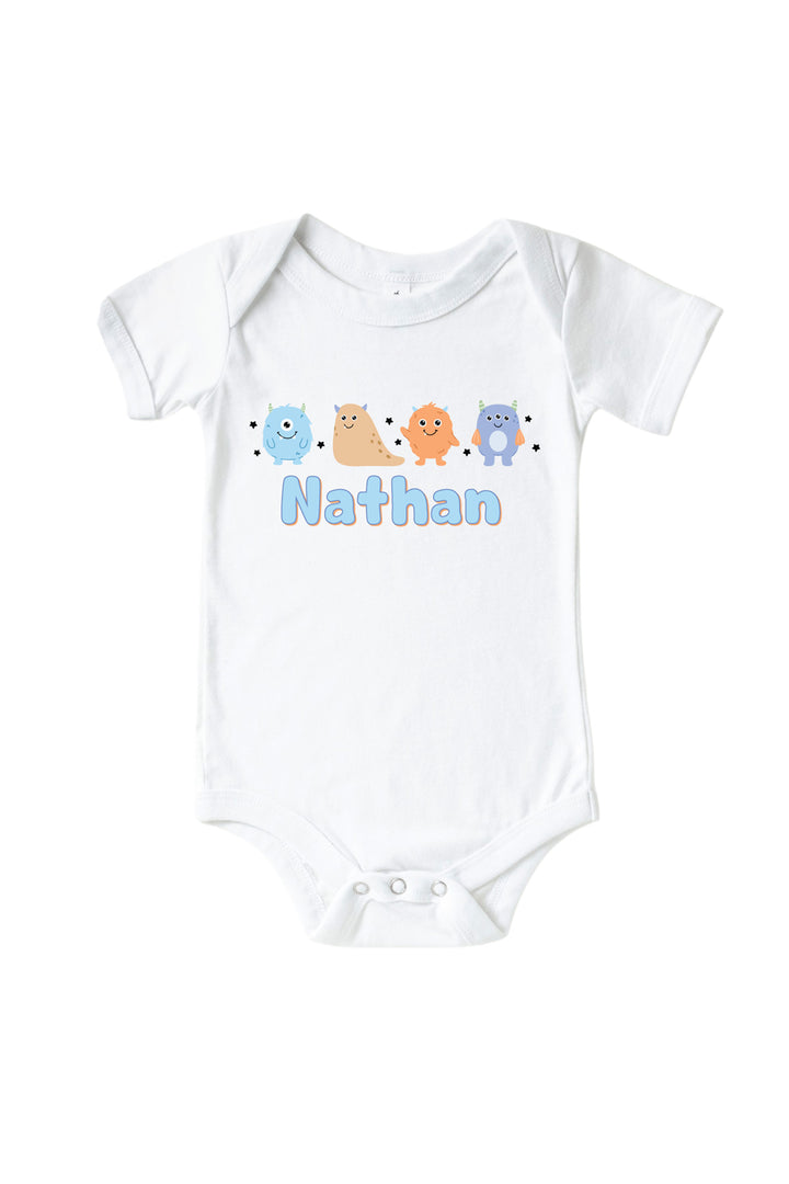 Caden Lane white baby onesie personalized with "Nathan" in blue lettering, featuring blue, tan, orange, and purple cartoon monsters and stars
