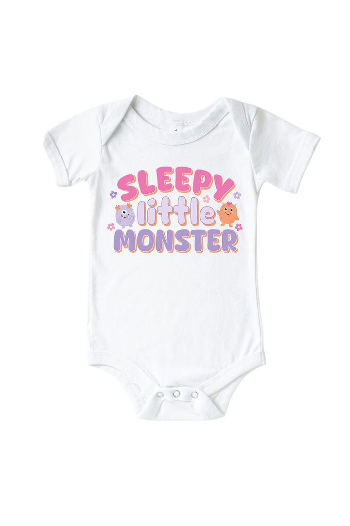 Caden Lane white baby onesie with "Sleepy Little Monster" graphic in pink and purple lettering, featuring purple and orange cartoon monsters and flowers
