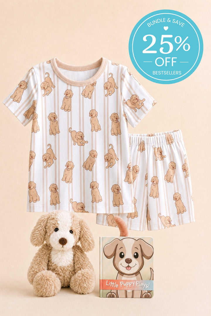 Flat lay of a Caden Lane short-sleeve pajama set in a striped puppy print, paired with a plush puppy and a "Little Puppy Plays!" board book.