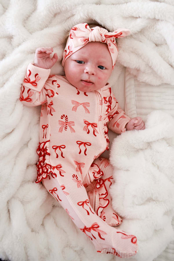 Baby wearing the Caden Lane Peppermint Bows Bamboo Waffle Zipper Ruffle Footie with matching bow headwrap for a cozy Christmas holiday look.