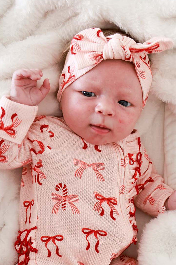 Baby girl dressed in Caden Lane Christmas bamboo waffle pajamas with Peppermint Bows print and coordinating headwrap.