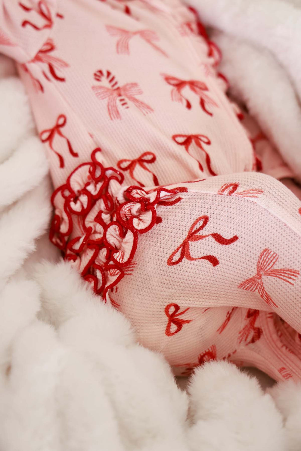 Close-up of the Caden Lane Peppermint Bows Bamboo Waffle Zipper Ruffle Footie showcasing festive bow print, candy cane details, and signature ruffle trim.