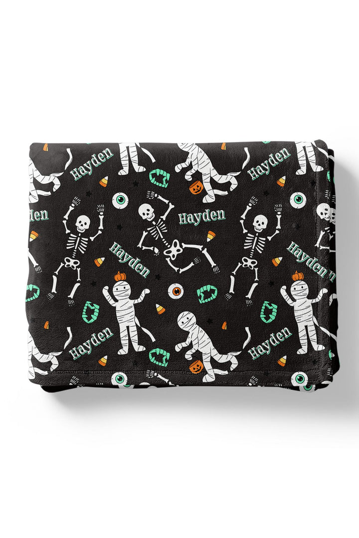 Folded black blanket personalized with the name 'Hayden' and Halloween skeleton and mummy graphics on a white background.