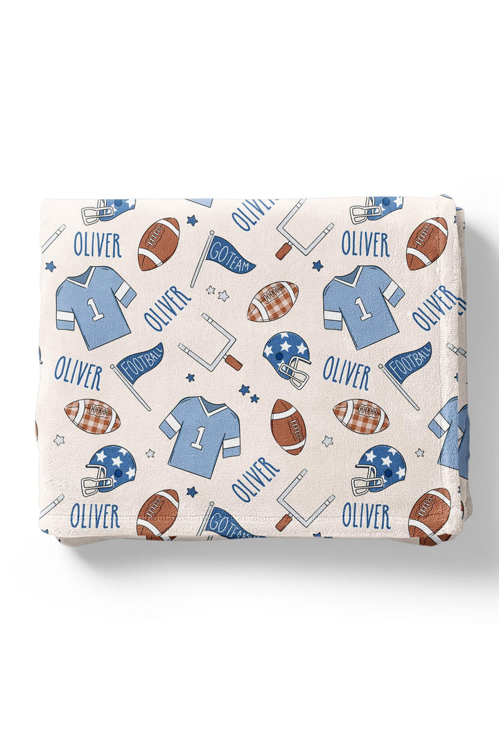 Caden Lane personalized baby blanket in blue football print, folded, featuring footballs, jerseys, helmets, goal posts, and the custom name "Oliver.